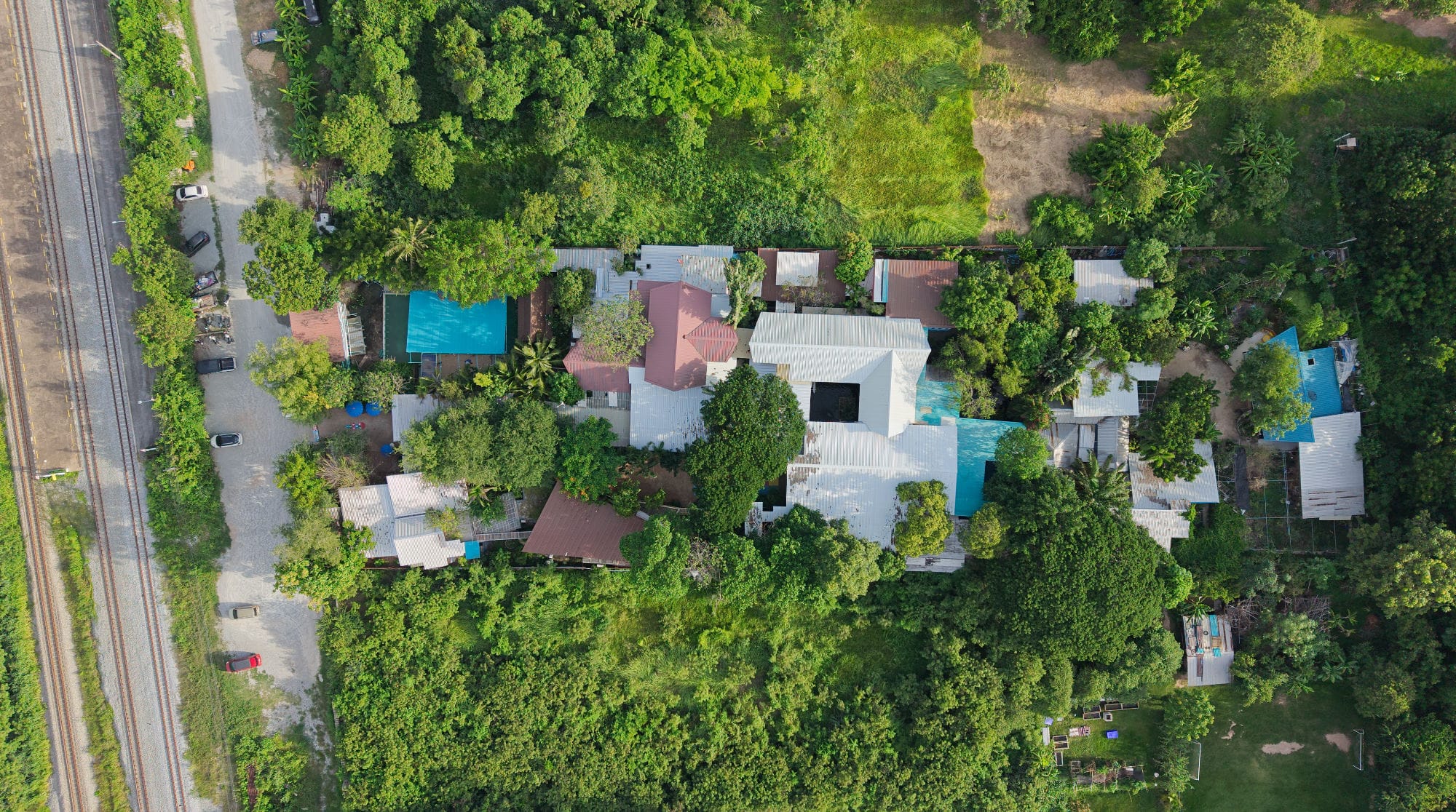 Aerial view of the Mosaic School campus with tree-shaded buildings, a pool and a railway line alongside