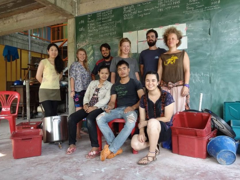 Nine volunteers and staff posing together in front of a chalkboard in the Daruma classroom